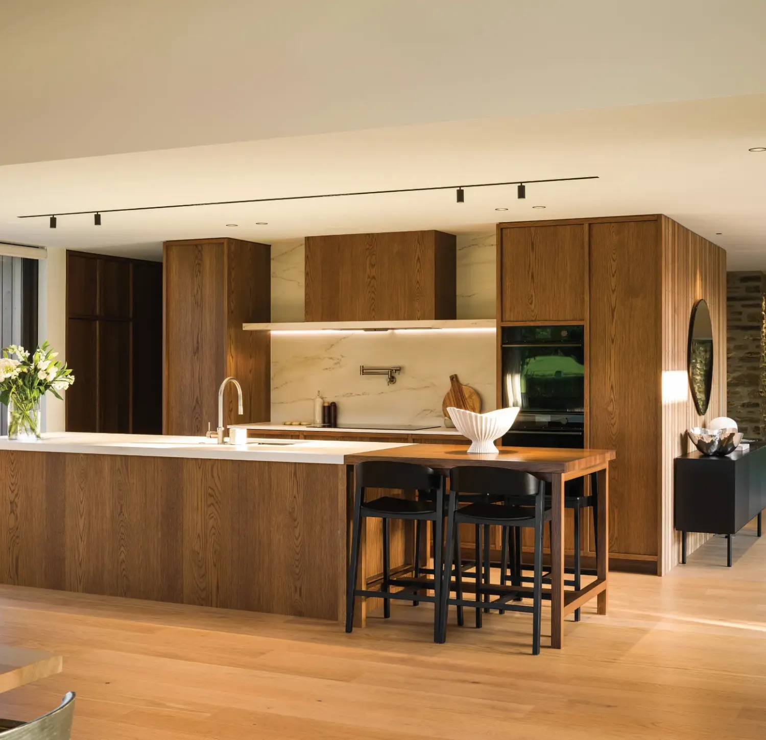 Open-plan kitchen with dark oak cabinetry, marble splashback and breakfast bar, light timber floors – architectural design by Chilton + Mayne